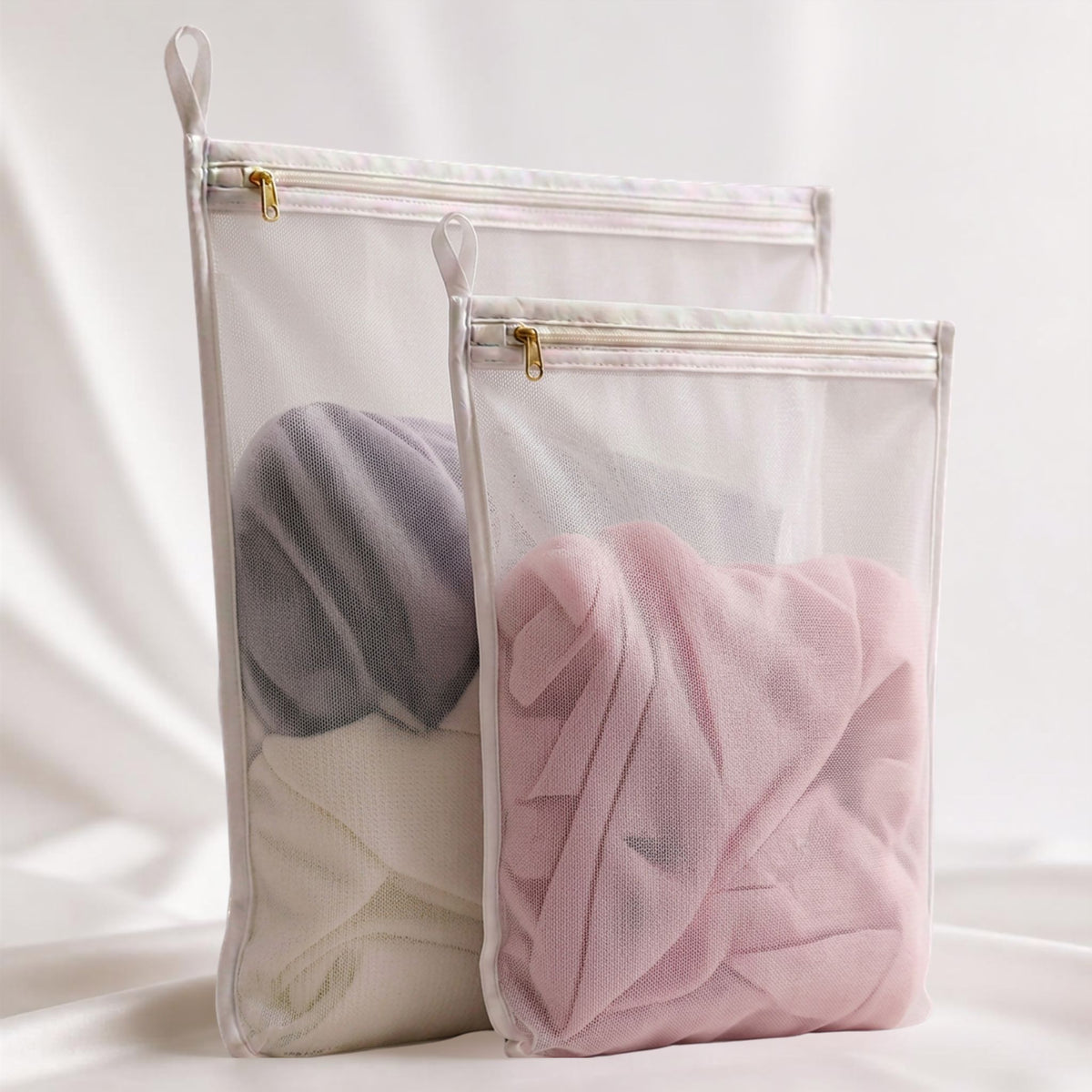 Two RYVENA mesh wash bags holding folded grey and blush silk, zips closed