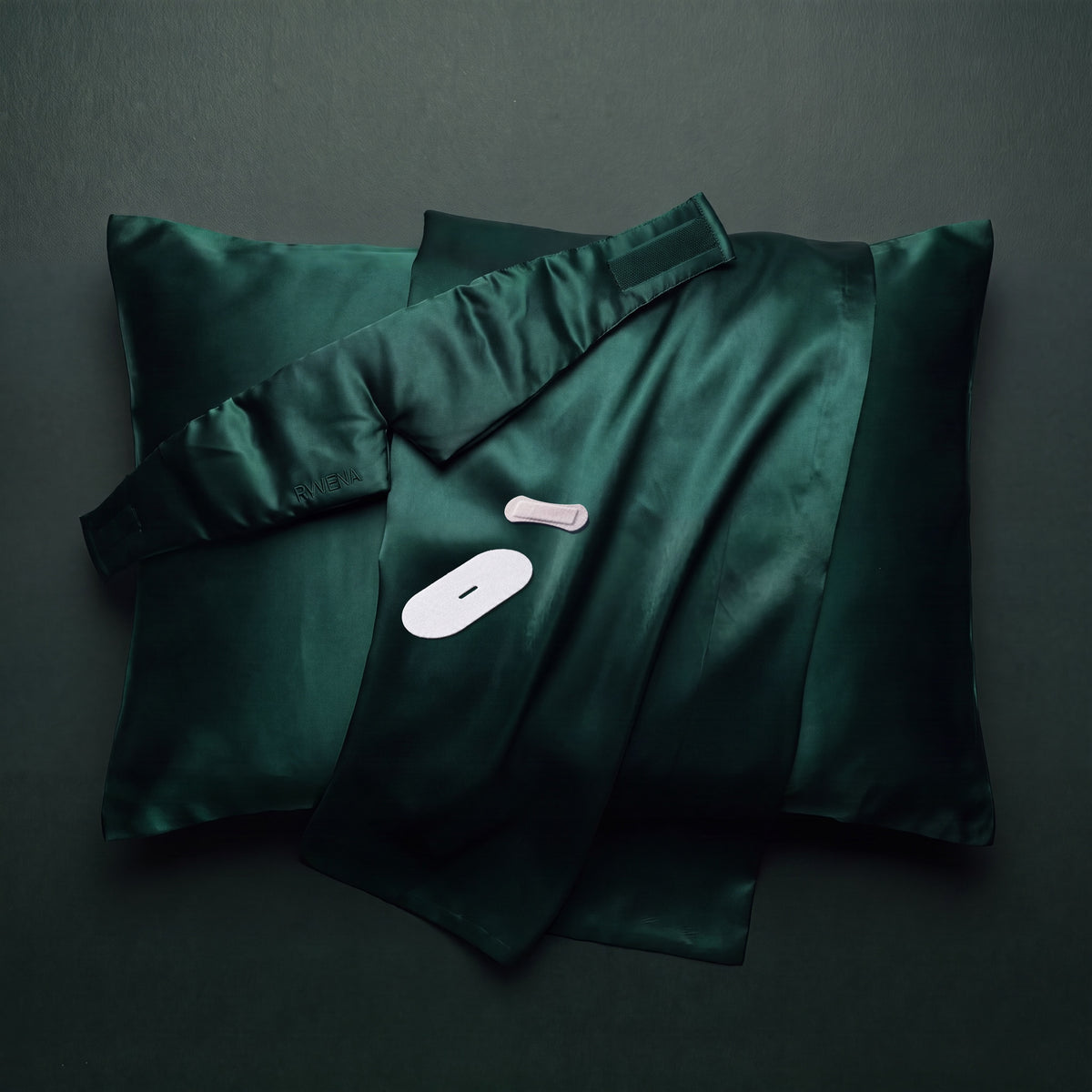 Overhead flat lay of emerald silk, the RYVENA mask, a white nose strip and mouth tape