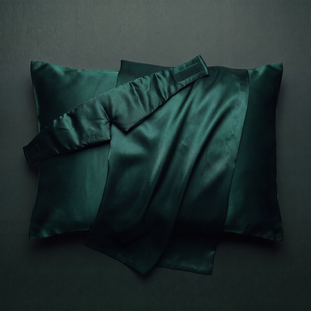 RYVENA emerald green silk sleep mask resting on a silk pillowcase