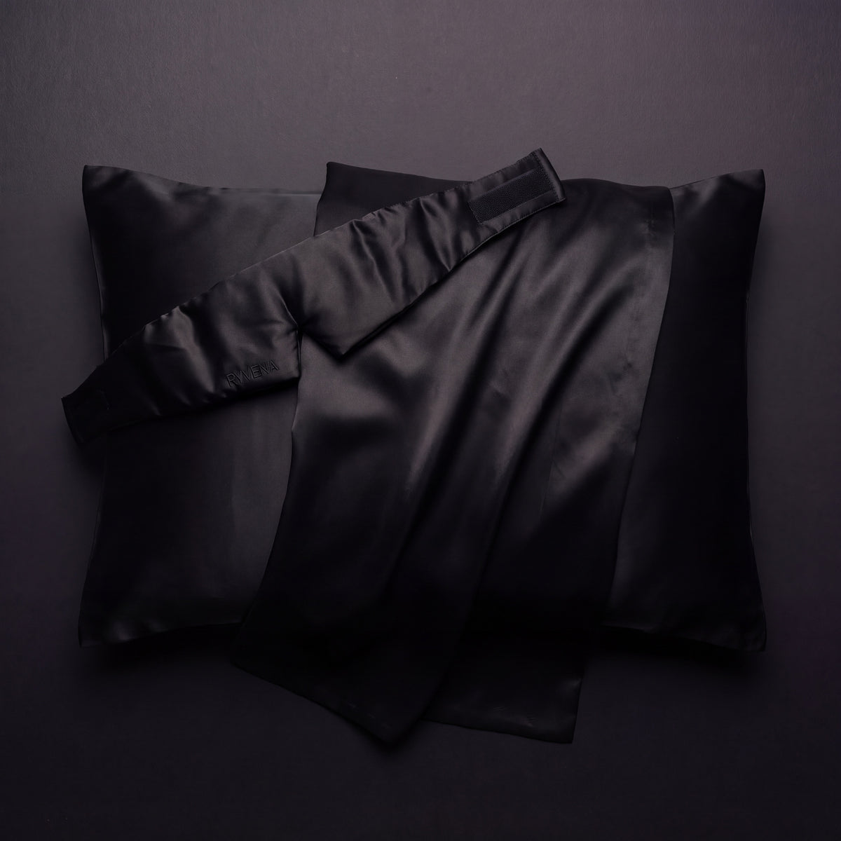 RYVENA deep black silk sleep mask resting on a silk pillowcase