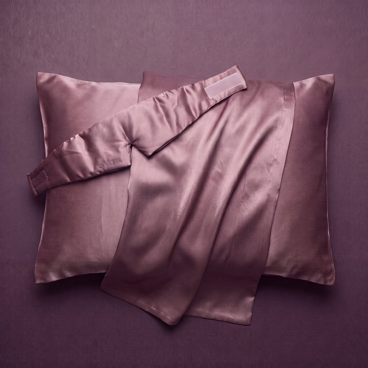 RYVENA blush pink silk sleep mask resting on a silk pillowcase